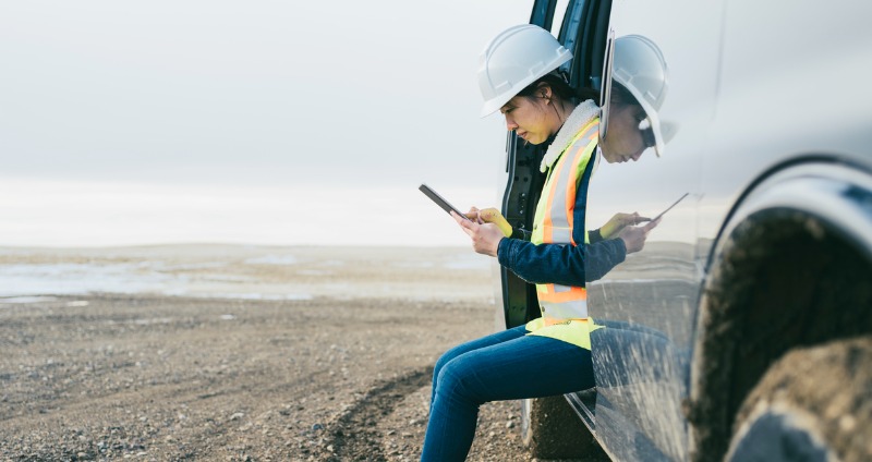 Woman using her device to stay connected while sitting in a car and working remotely.