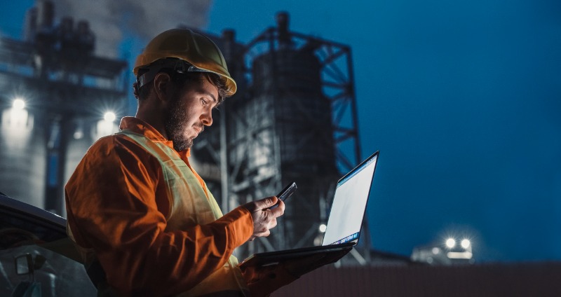 Engineer standing in front of a manufacturing plant using Li-Fi technology on his rugged device.