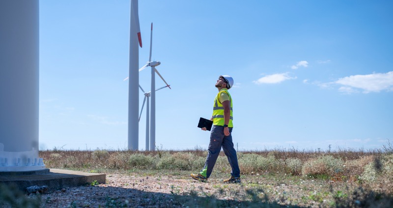 Man assessing wind turbines while using rugged tablet technology to manage work priorities out in the field.