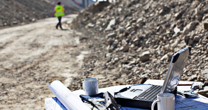 Man working on a rugged laptop on a rock, in nature