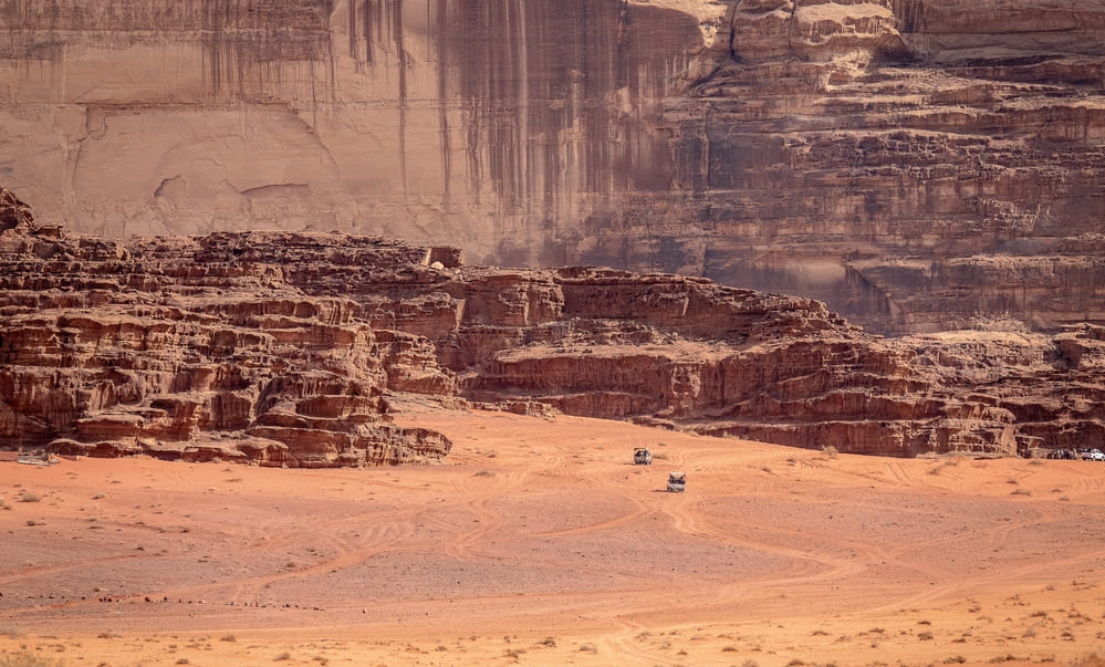 Rugged vehicles travelling through a remote desert landscape with rocky cliffs, representing harsh environments where rugged tablets are used