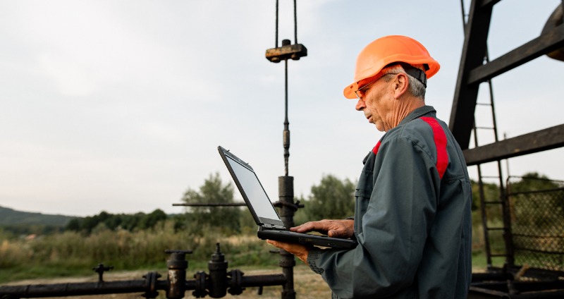 Military man using a rugged laptop while holding a walkie-talkie during an outdoor military operation